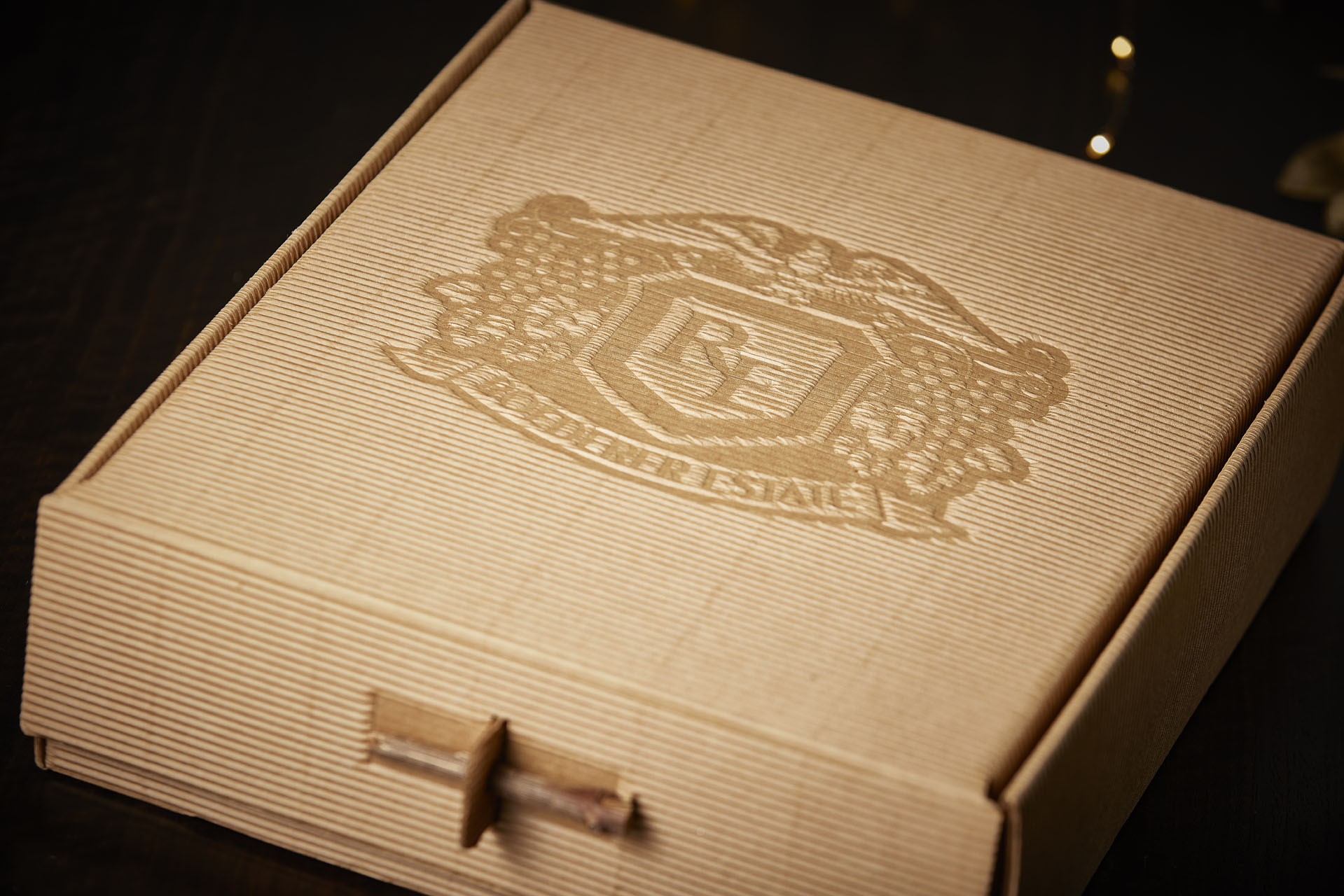 A cardboard box with an embossed crest featuring a shield and decorative elements. The words "Roederer Estate" are printed below the crest. The box has a textured finish and a pull tab for opening.